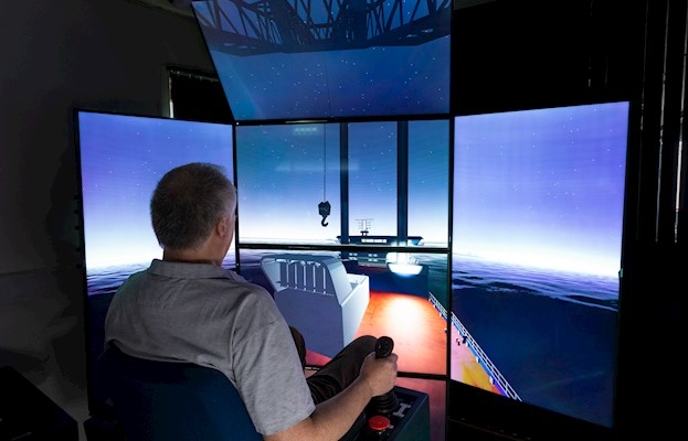 Photo 1: The new crane lifting simulator at our training facilities in Lyngby. The setup is equipped with crane training cubicle, 2 joysticks and 6 large LED screens providing a 180-degree view from the crane tower. To the left, the Jack-Up console and the DP console.