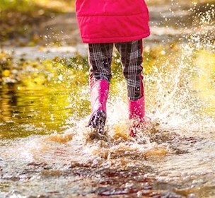 Child in pink gum boots jumping in a puddle